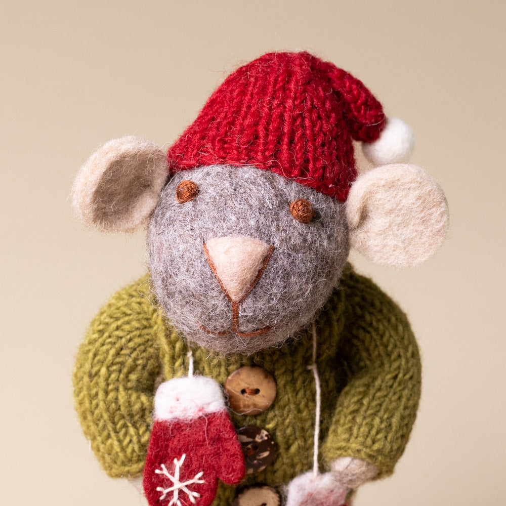 felted-grey-mouse-green-sweater-pink-skirt-and-mittens Knitted mouse toy wearing a red hat and green sweater on a beige background