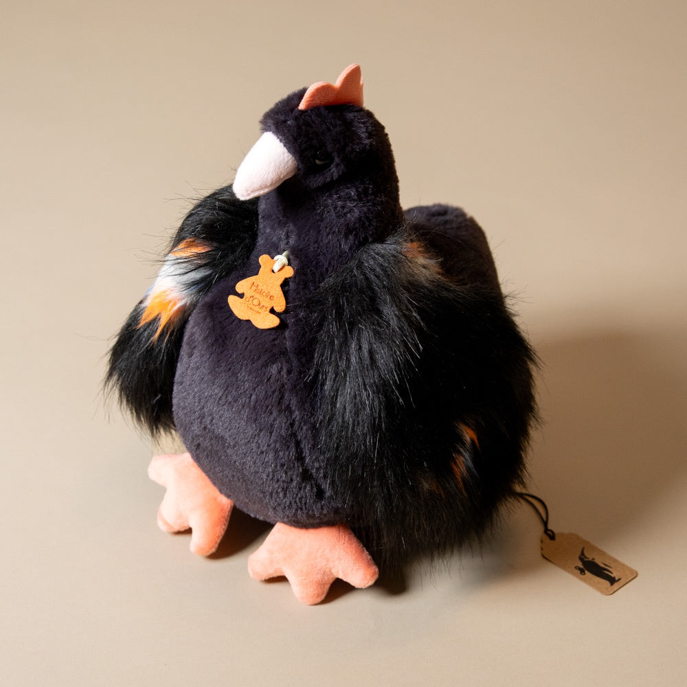 Black floofy-chicken-plush toy with orange accents on a beige background