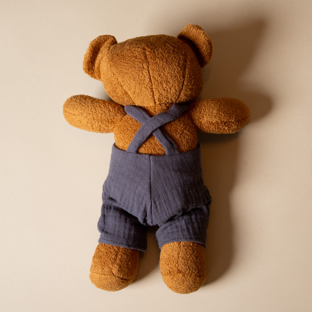 back gabin-the Brown teddy bear wearing blue overalls on a beige background