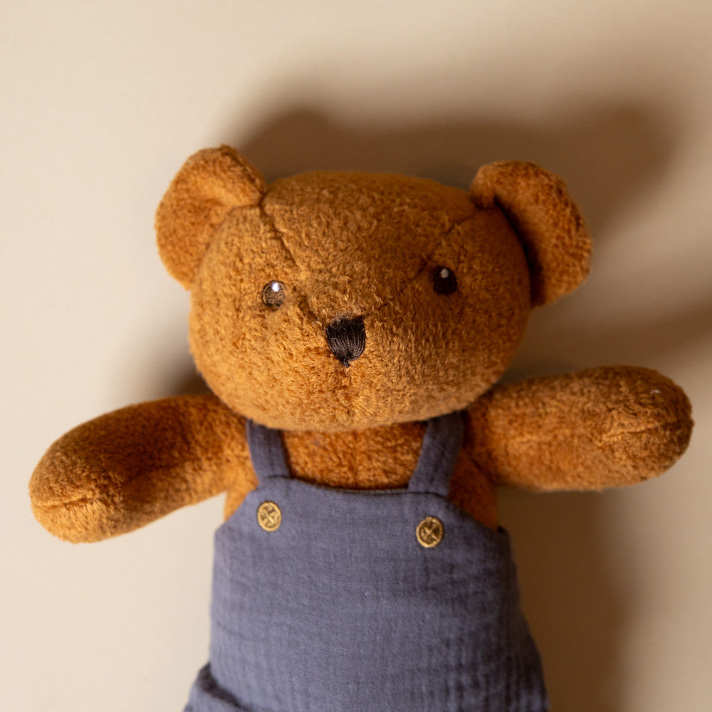 gabin-the-Brown teddy bear wearing a blue overalls against a beige background