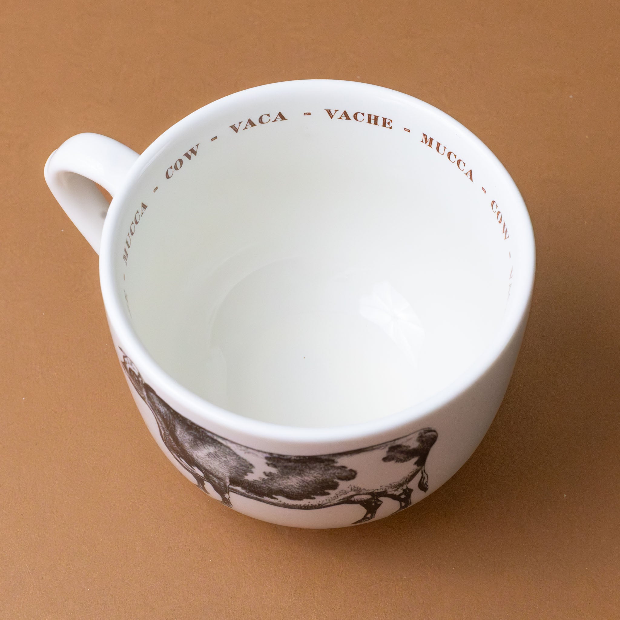 white-cup-grande-stoneware-cup-black-illustration-of-cow-with-the-word-cow-in-red-in-several-languages-on-interior