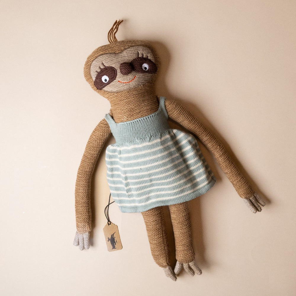hanna-sloth Knitted sloth toy wearing a striped dress on a beige background