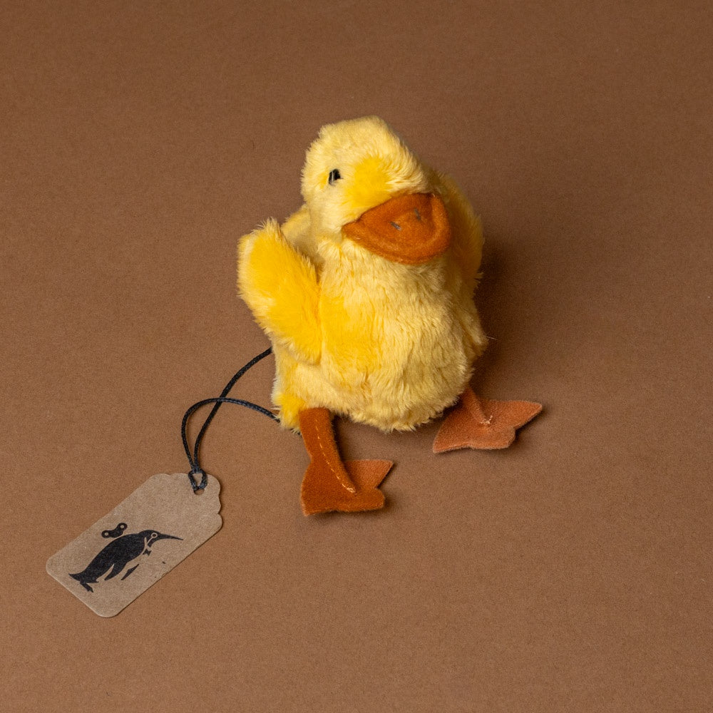 little-duck-chick-finger-puppet Yellow plush duck with a tag on a brown background