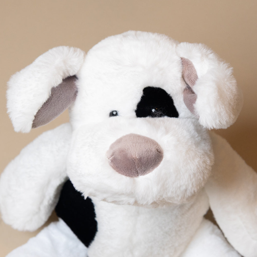 Close-up of a plush noopy-dog toy with a white face and black spots on a beige background