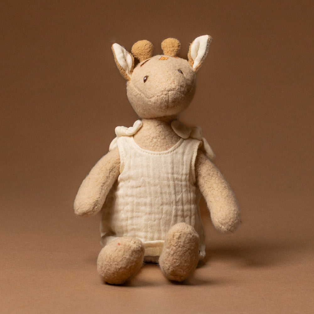 organic-cotton-leonie-giraffe--petite Stuffed toy in a white outfit on a brown background