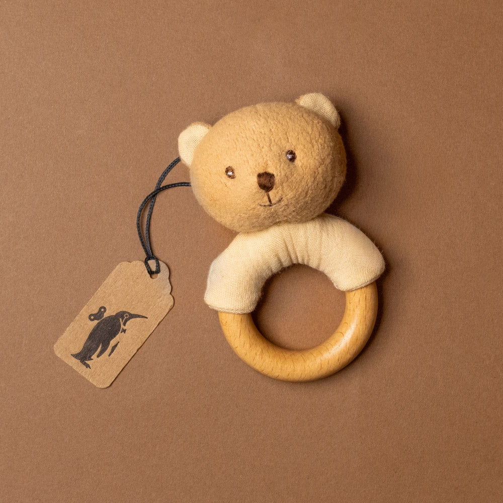 organic-cotton-marcel-bear-rattle Teddy bear-shaped wooden ring with a tag on a brown background