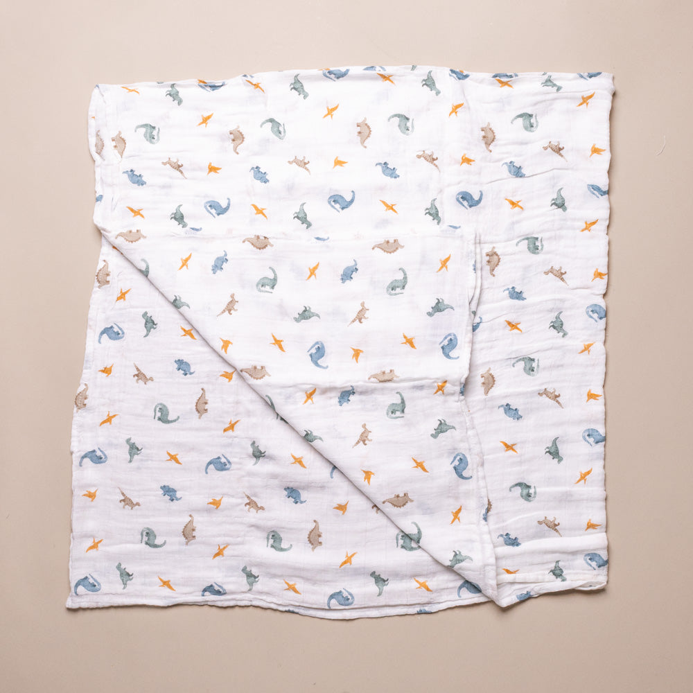 organic-cotton-muslin-swaddle-little-dinos Folded baby blanket with dino pattern on a beige background