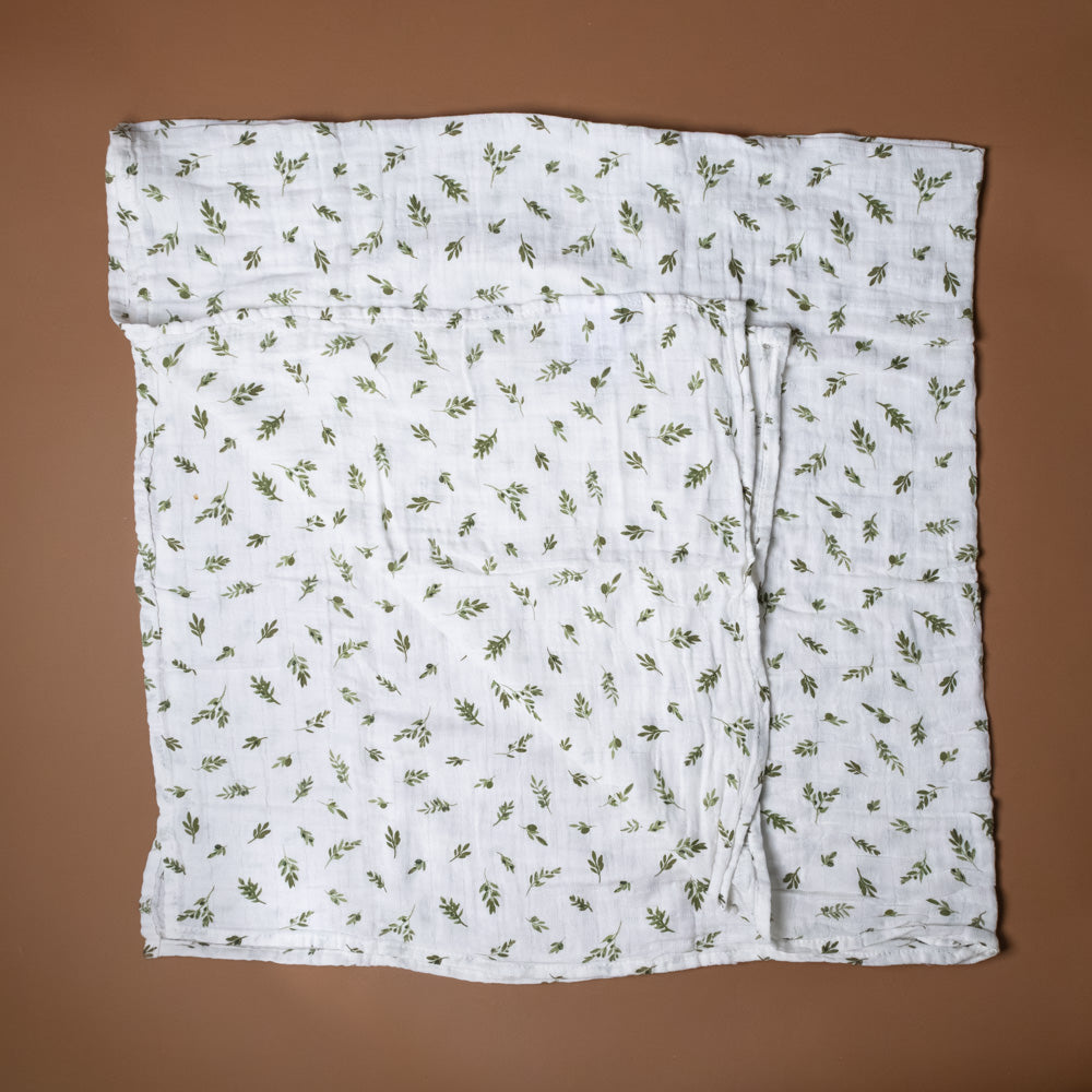 organic-cotton-muslin-swaddle-olive-branch White fabric with green leaf pattern on a brown background