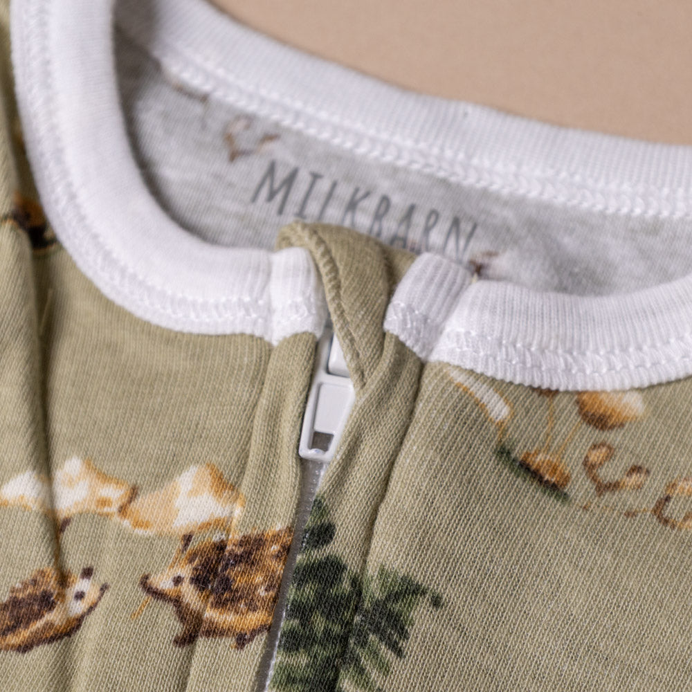 organic-cotton-zipper-pajamas-forest-party Close-up of a green baby romper with animal prints and 'Milkbarn' label.