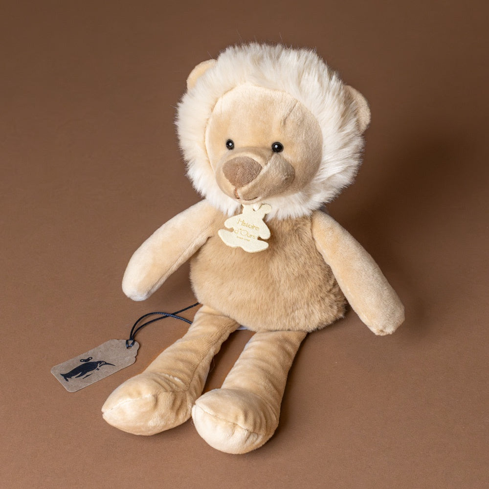 petite-lion-cub Plush lion toy with a tag on a brown background
