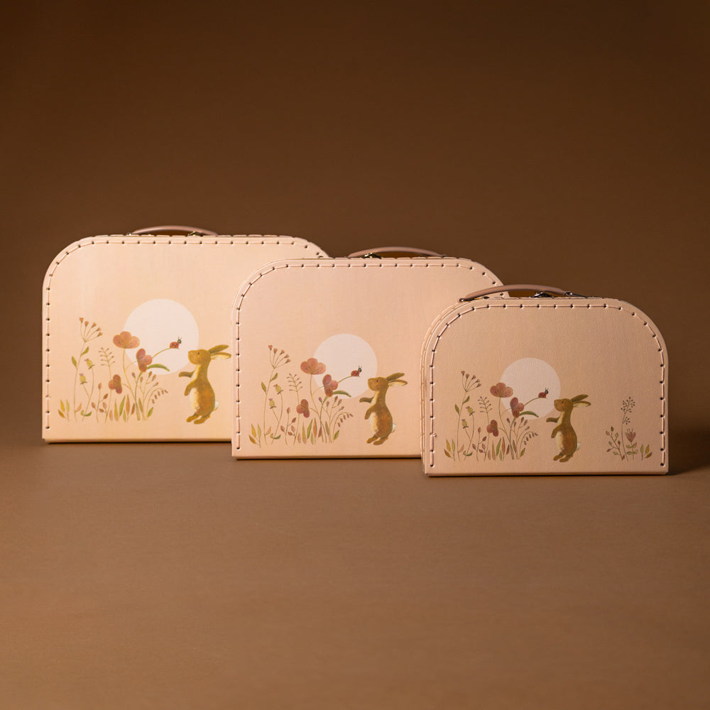 rabbit-family-suitcase-large Three beige pouches with rabbit and flower designs on a brown background