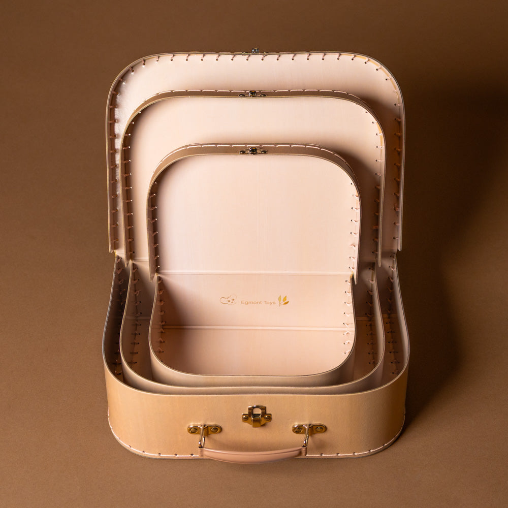 rabbit-family-suitcase-large Set of three blush suitcases nested with gold accents on a brown background