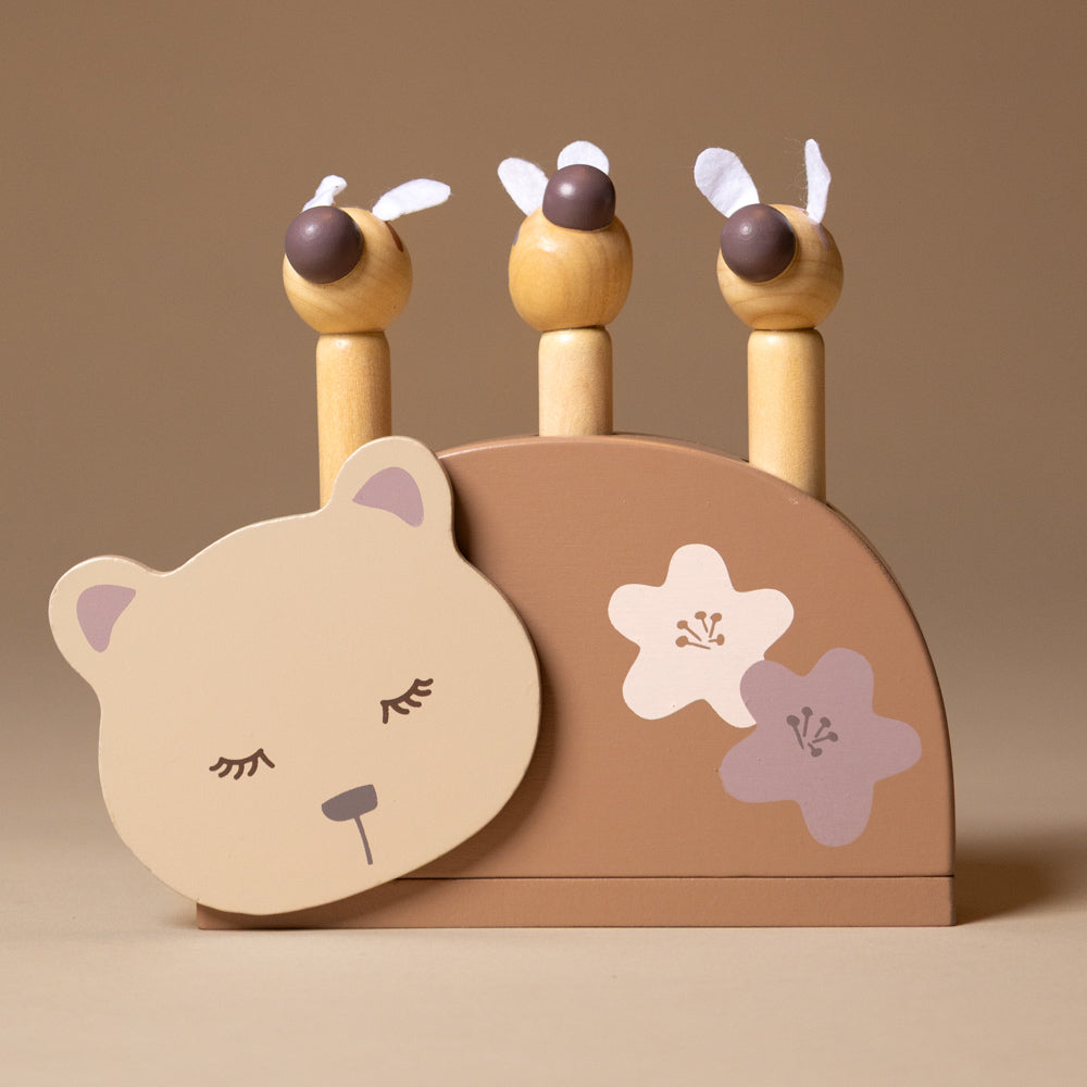 sleeping-bear-and-the-bees Wooden toy with bear face and flower designs on a beige background