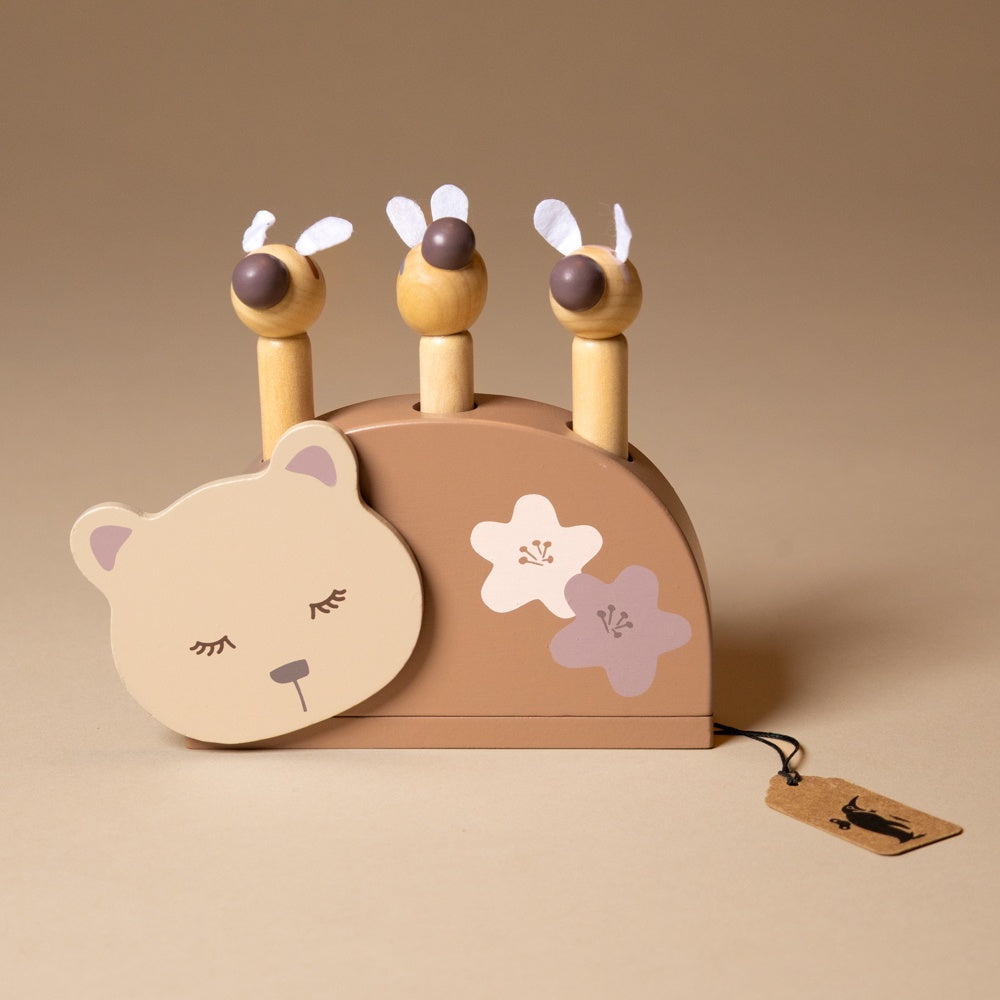sleeping-bear-and-the-bees Wooden toy with bear face and flower designs on a beige background