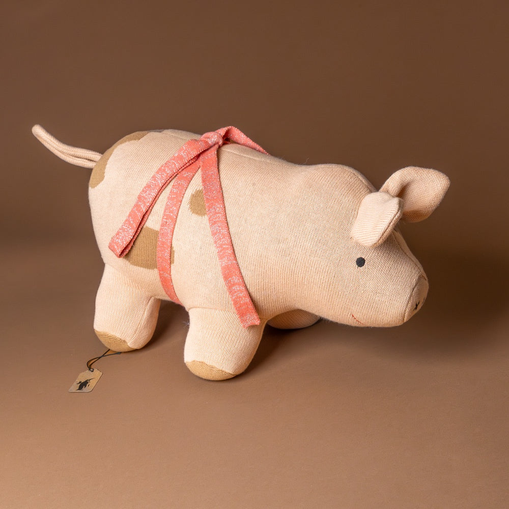 sofie-pig Stuffed animal toy resembling a pig with a pink ribbon on a brown background