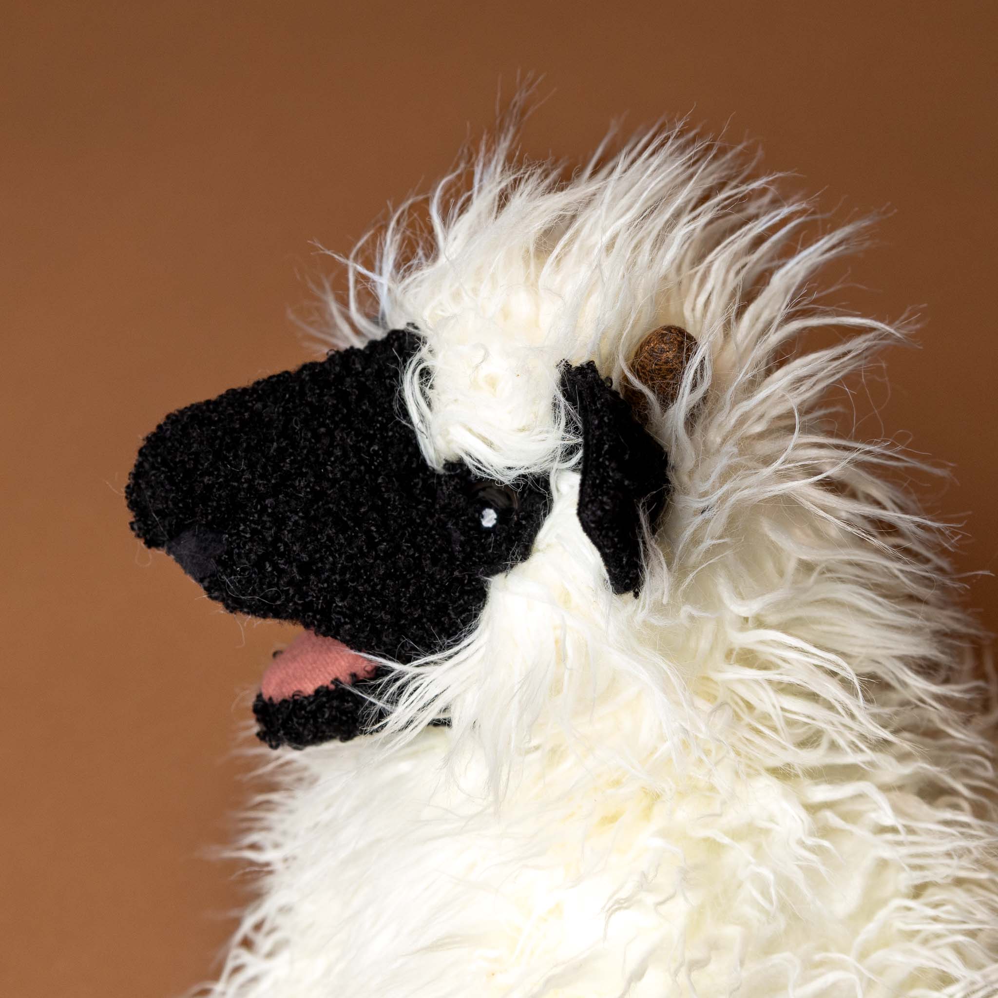 valais-black-nose-sheep-hand-puppet Close-up of a fluffy white animal with black face on a brown background