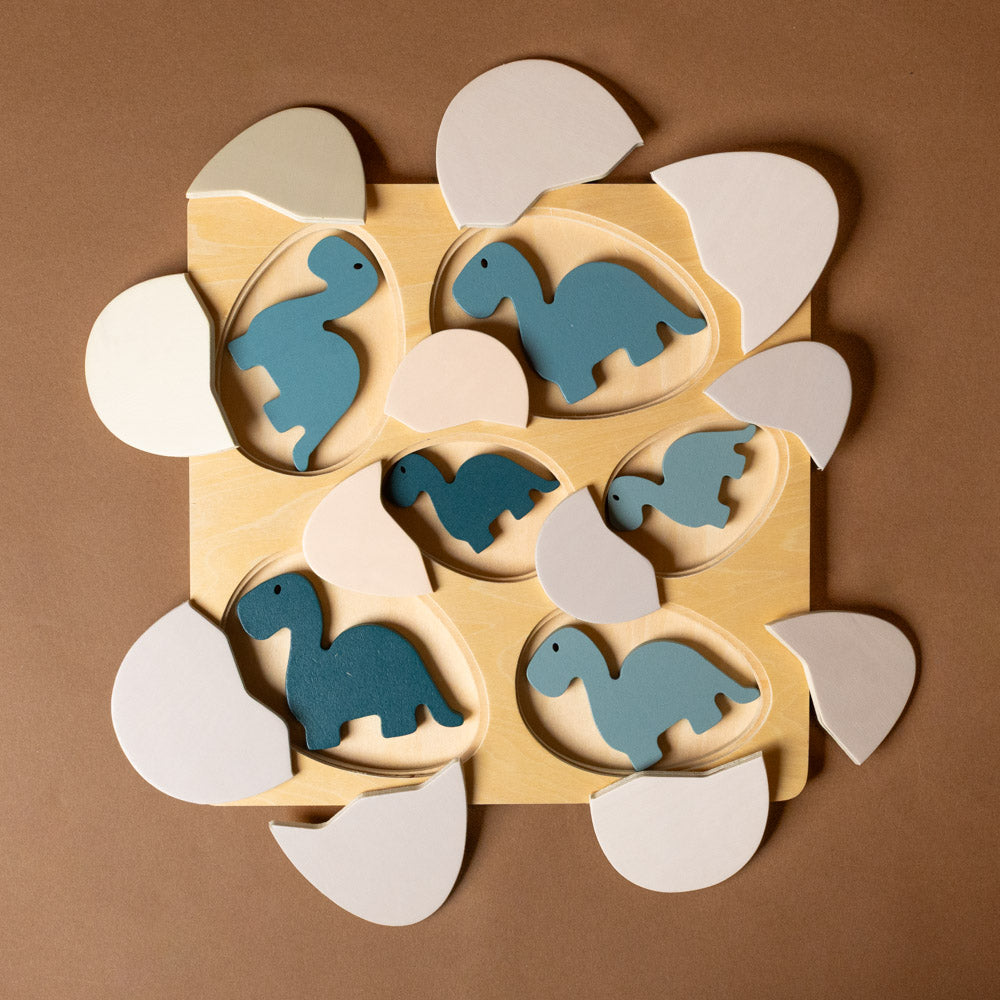 wooden-dino-eggs-puzzle Wooden puzzle with blue dinosaur shapes on a brown background