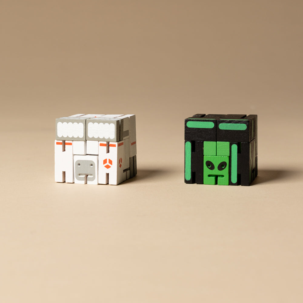 wooden-micro-cubebot-space-buddies-set Two toy blocks, one white with gray accents and the other black with green accents, on a beige background.