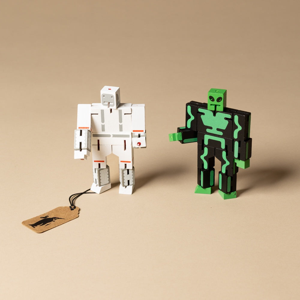 wooden-micro-cubebot-space-buddies-set  Two robot toy figures, one white and one black with green accents, on a beige background.